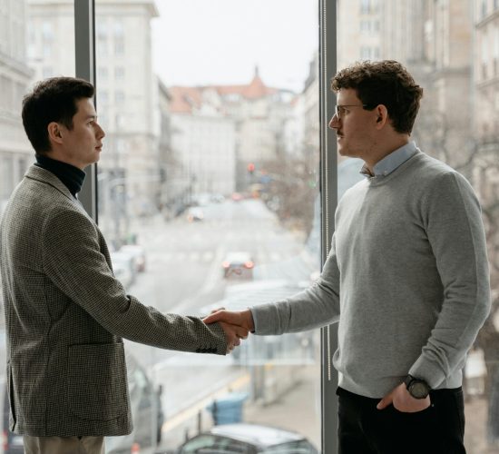 Businessmen in a modern office setting, sealing a deal with a handshake against a city backdrop.
